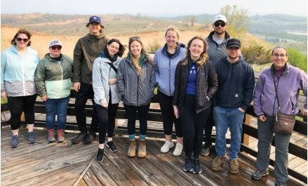 A group of people standing on a wooden platform with hills in the background.